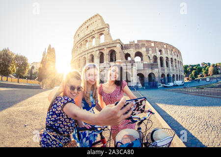 Drei glückliche junge Frauen Freunde Touristen mit Fahrrädern unter selfies am Kolosseum in Rom, Italien bei Sonnenaufgang. Stockfoto