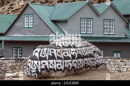 Alte buddhistische Mani Stein mit Gravierten heilige Mantra "Om Mani Padme Hum" vor dem Hintergrund der typischen Häuser in die hohen Berge des Himalaya Stockfoto