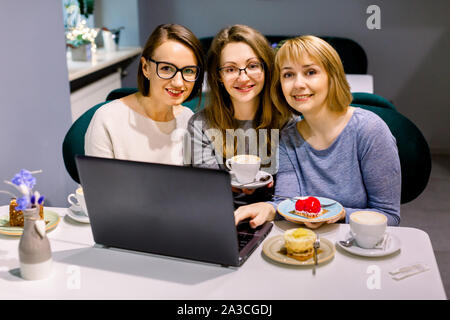 Frauen Freunde auf Kamera im Cafe, essen leckere Desserts und trinken Tee, mit Laptop für die Arbeit. Frauen blogger Freiberufler im Cafe arbeiten Stockfoto