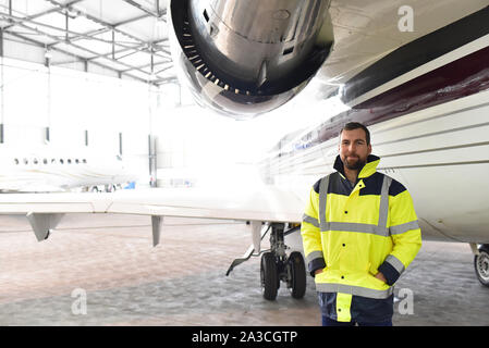 Portrait einer flugzeugmechaniker in einem Hangar mit Jets am Flughafen - Kontrolle der Flugzeuge für Sicherheit und Technische Funktion Stockfoto