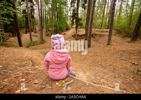 Ansicht der Rückseite ein 4 Jahre altes Kind Mädchen in rosa warme Kleidung sitzt in einem Wald auf einem Stimmungsvollen Tag im Oktober in Deutschland und mit einer Unterbrechung und Wat Stockfoto