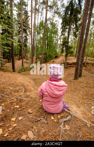 Ansicht der Rückseite ein 4 Jahre altes Kind Mädchen in rosa warme Kleidung sitzt in einem Wald auf einem Stimmungsvollen Tag im Oktober in Deutschland und mit einer Unterbrechung und Wat Stockfoto