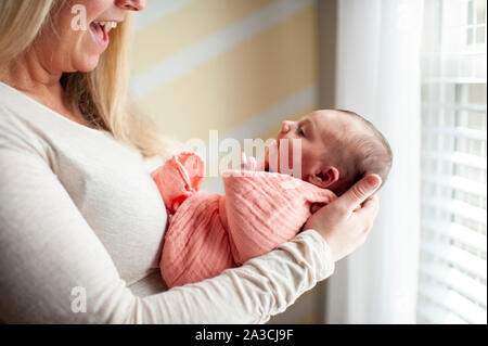 Mutter lächelnd an ihrer neugeborenen Tochter, während in ihren Armen zu Hause Stockfoto