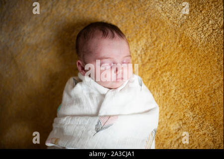 Neugeborene Mädchen eingehüllt in Decke schlafen zu Hause auf gelben Teppich Stockfoto