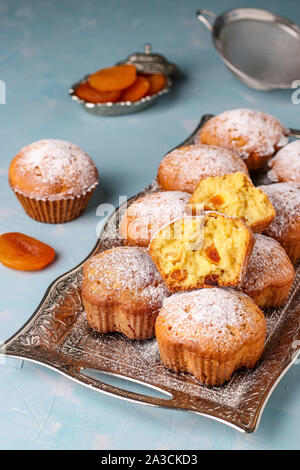 Hausgemachte Muffins mit getrockneten Aprikosen bestreut mit Puderzucker auf einem Tablett auf einem hellblauen Hintergrund, vertikale Ausrichtung, Ansicht von oben Stockfoto