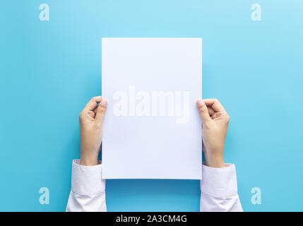 Die Hände schließen Holding leere weiße Leere schreiben Papierformat A4 für Flyer oder Einladung mock up auf einem blauen Hintergrund. Stockfoto