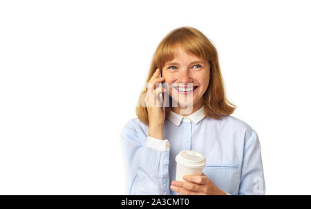 Ginger-Kopf-Mädchen in lässigen Hemd gekleidet Gespräch am Telefon und lächelnd hält eine Tasse Kaffee. Isolierter, weißer Hintergrund, Kopierbereich. Stockfoto