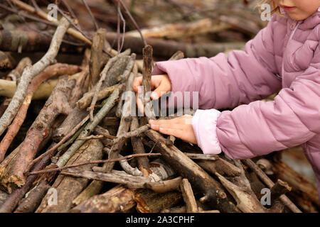 Den mittleren Abschnitt der ein 4 Jahre altes Kind Mädchen in Lila warme Kleidung etwas zu bauen mit Holz in den Wald zu einem Stimmungsvollen Tag im Oktober in Stockfoto