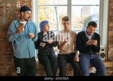 Gruppe von Happy kaukasischen jungen Leute, hinter dem Fenster. Gemeinsame Nutzung einer News, Fotos oder Videos von Smartphones, reden oder spielen und Spaß haben. Soziale Medien, moderne Technologien. Stockfoto