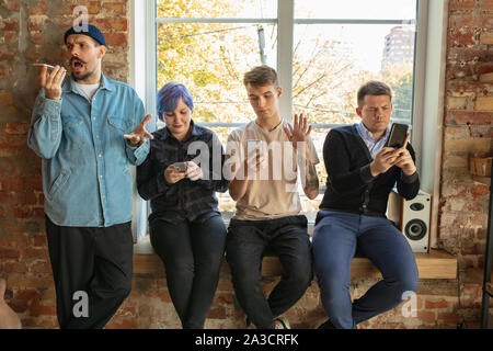 Gruppe von Happy kaukasischen jungen Leute, hinter dem Fenster. Gemeinsame Nutzung einer News, Fotos oder Videos von Smartphones, reden oder spielen und Spaß haben. Soziale Medien, moderne Technologien. Stockfoto