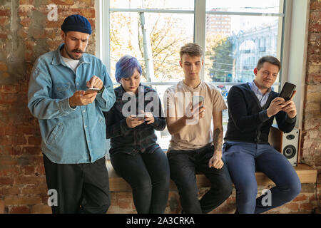 Gruppe von Happy kaukasischen jungen Leute, hinter dem Fenster. Gemeinsame Nutzung einer News, Fotos oder Videos von Smartphones, reden oder spielen und Spaß haben. Soziale Medien, moderne Technologien. Stockfoto