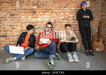 Gruppe von Happy kaukasischen jungen Menschen hinter der Mauer. Gemeinsame Nutzung einer News, Fotos oder Videos von Smartphones, Laptops oder Tabletten, spielen und Spaß haben. Soziale Medien, moderne Technologien. Stockfoto