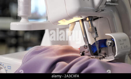 Verarbeitung von Gewebe aus Stoff. Näherin an der Nähmaschine die "Nähte Nähte mit Geradstich auf lila Tuch, Hände, Nahaufnahme. Bekleidung Schneiderei business herstellen. Stockfoto