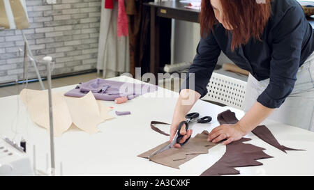 Zuschneiden und Nähen Produkte in Tailoring business. Maßgeschneiderte Frau schneiden Details aus Stoff arbeitet in Schneiderei business. Schneiden mit Schere Zick-zack. Schneiderin erstellen Neues Produkt. Stockfoto