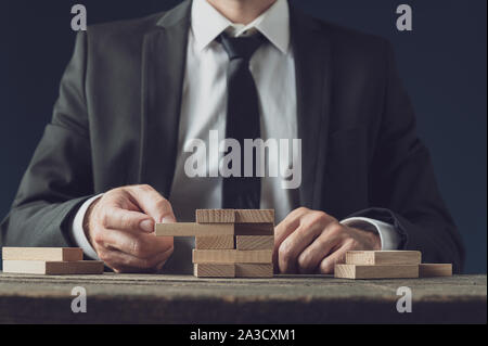 Vorderansicht des Geschäftsmannes an seinem Schreibtisch einen der hölzernen Stapel Spielsteine in einem konzeptionellen Bild der Geschäftsstrategie und Idee. Stockfoto