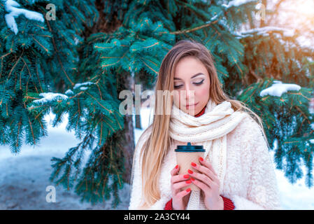 Schöne Mädchen Daunenjacke schal Winter verschneite Park, Hintergrund weiß Schnee, Tasse mit heißem Kaffee trinken Kaffee Fichte, wärmt, entspannt Winter Resort Stockfoto