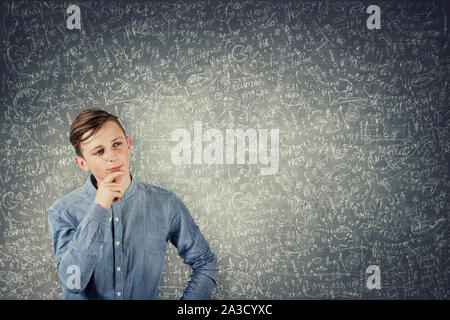 Smart Teenager denken, hält die Hand unter das Kinn, steht vor einer Tafel die Lösung schwer Mathematik Berechnung und Gleichungen. Verwirrte Schüler Stockfoto