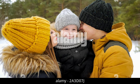 Portrait von Happy Family im Winter Tag. Mama und Papa sind Kuscheln küssen und ihren kleinen Sohn in Winter Park. Familie schöne Momente. Stockfoto