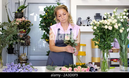 Professionelle Floristen bei der Arbeit im Blumengeschäft. Frau in Uniform stehen in der Nähe des Tisches und macht Blumenstrauß Stockfoto