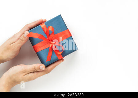 Blauen Geschenkbox mit roter Schleife in der womans Hände auf weißem Hintergrund. Ansicht von oben. Copyspace Stockfoto