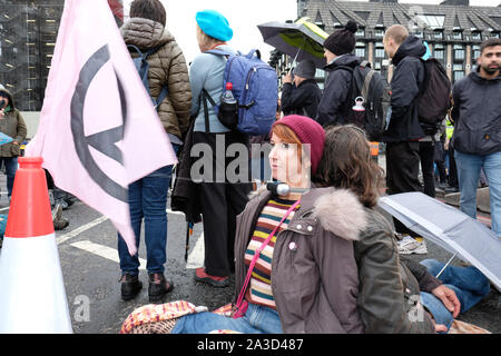 Westminster, London, UK - Montag, 7. Oktober 2019 - Zwei Aussterben Rebellion XR Demonstranten haben ihre Hälse zusammen verriegelt und im Nieselregen auf die Westminster Bridge sitzen. Foto Steven Mai/Alamy leben Nachrichten Stockfoto