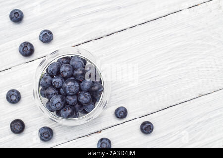 Heidelbeeren im Glasplatte und Beeren sind auf einem weißen Tisch verstreut. Ansicht von oben Stockfoto