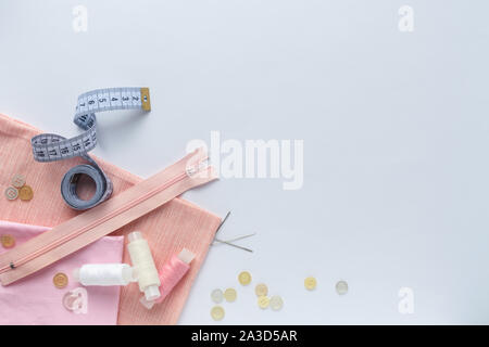 Nähzubehör und rosa Stoff auf einem weißen Hintergrund. Stoff, Nähgarne, Nadel, Tasten und nähen Zentimeter. top Aussicht, flatlay Stockfoto