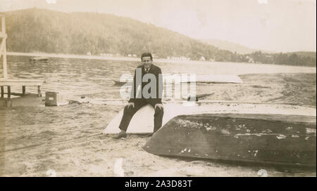 Antike Oktober 12, 1945 Foto, Mann auf Ruderboote sitzend auf dem Strand in der Nähe des Bungalow Dorf am Newfound Lake, New Hampshire. Quelle: original Foto Stockfoto