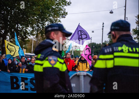 Zwei niederländische Polizisten sprechen, bevor die Demonstranten halten ein Banner und Flaggen während der Demonstration. Für 2 Wochen, Aussterben Rebellion und verwandter Bewegungen werden in den großen Städten auf der ganzen Welt sammeln und weiterhin rebellieren gegen die Regierungen der Welt für ihre kriminellen Untätigkeit auf das Klima und die ökologische Krise zu. XR Klima Aktivisten in Amsterdam werden eine große Blockade über mehrere Tage auf der Museumbrug zu organisieren, vor dem Rijksmuseum. Von früh am Morgen, Hunderte von XR Aktivisten auf der Brücke, wo es eine sichtbare Polizeipräsenz. Die Umwelt Stockfoto