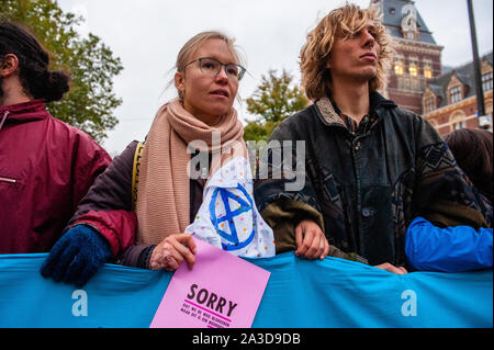 Ein XR Aktivist hält eine XR Flyer während der Demonstration. Für 2 Wochen, Aussterben Rebellion und verwandter Bewegungen werden in den großen Städten auf der ganzen Welt sammeln und weiterhin rebellieren gegen die Regierungen der Welt für ihre kriminellen Untätigkeit auf das Klima und die ökologische Krise zu. XR Klima Aktivisten in Amsterdam werden eine große Blockade über mehrere Tage auf der Museumbrug zu organisieren, vor dem Rijksmuseum. Von früh am Morgen, Hunderte von XR Aktivisten zeigte auf der Brücke, wo es mit einem sichtbaren polizeilichen Präsenz. Die Umweltorganisation aussterben Rebellion will die Du Stockfoto