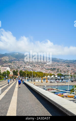 Funchal, Madeira, Portugal - 14.September 2019: Hafenpromenade in der Hauptstadt der portugiesischen Insel. Die Stadt auf dem Hügel im Hintergrund. Die Menschen auf der Straße, das tägliche Leben. Hafen, Marina. Stockfoto