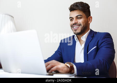 Fröhlicher junger Geschäftsmann arbeiten mit Laptop im Hotel Zimmer Stockfoto