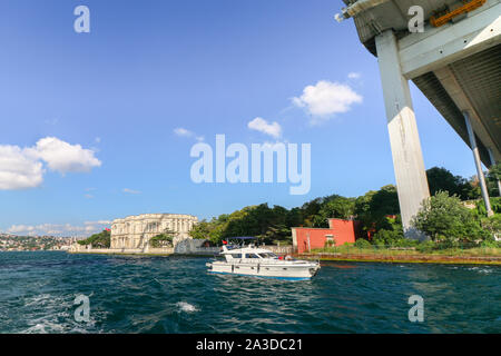 Die Bosporus-Brücke von unten und der Beylerbeyi-Palast im Hintergrund an einem sonnigen Sommertag. Weekender-Boot fährt unter. Stockfoto