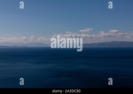 Hellen blauen Ozean mit Berge und Wolken im Hintergrund und die Sonne auf dem Wasser. Stockfoto