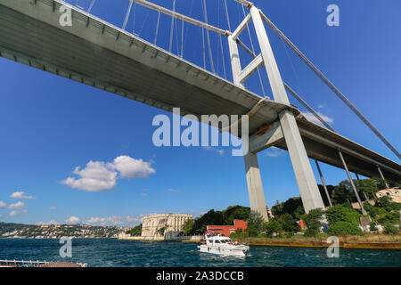 Die Bosporus-Brücke von unten und der Beylerbeyi-Palast im Hintergrund an einem sonnigen Sommertag. Weekender-Boot fährt unter. Stockfoto