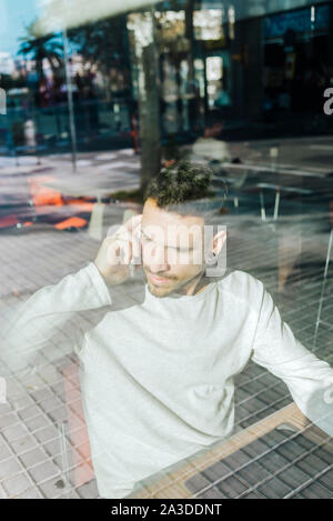 Nachdenklicher junger Mann mit Telefon im Coffee Shop Stockfoto