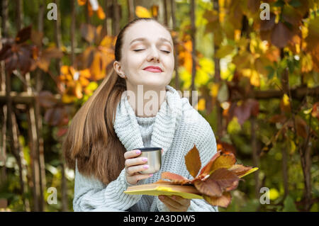 Das Mädchen entspannt und trinkt Kaffee aus der Thermoskanne. Herbst im Park. Life style Konzept, Herbst, Entspannen und Lesen. Stockfoto