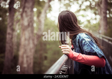 Androgyne Frau beugt sich über Geländer in Treetop Walk durch den Wald Stockfoto