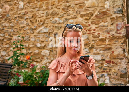 Freuen weiblich im Sommer Sie Ihr Smartphone während der Rest der mittelalterlichen Stadtmauer in Italien Kleid Stockfoto