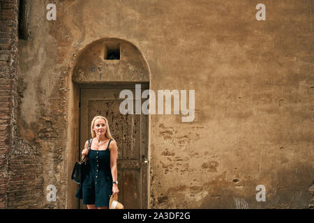 Frau in Schwarz sundress mit fairen Haar Ausflüge in die Umgebung von Stone grunge Gebäude mit Holztür in der Toskana Italien Stockfoto