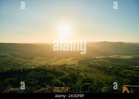 Luftaufnahme der atemberaubenden szenischen Hügel Landschaft mit grünen üppigen Wäldern Feldern Gebäude und die Sonne in der Region Toskana in Italien Stockfoto