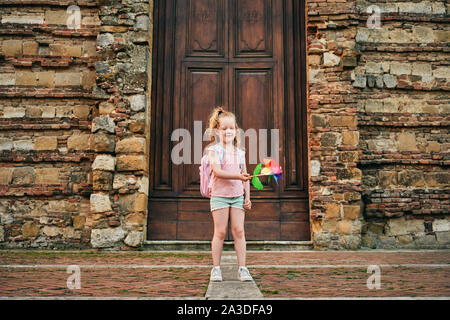 Adorable Reisen kid Winken mit bunten Papier Mühle stehen auf der Straße mit Holztür in alten Steinmauer in Toskana Italien Stockfoto