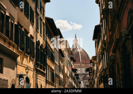 Verwitterte alte Gebäude auf einer schmalen Straße der Stadt gegen die Kuppel des im Alter von Kirche und blauem Himmel in der Toskana, Italien. Stockfoto