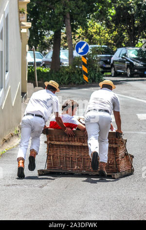 Monte, Madeira, Portugal - 14.September 2019: Weidenkorb Hundeschlittenfahrt mit Carreiros do Monte. Traditionelle Verkehrsmittel zu Funchal, jetzt eine touristische Attraktion. Menschen reiten bergab mit Treibern. Stockfoto