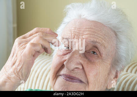 Eine ältere Frau Augentropfen, die in ihren Augen von sich selbst Stockfoto