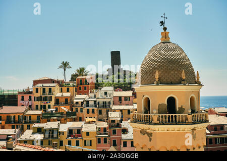 Ländliche Gemeinde am Hang des Hügels mit hellen Gebäude und Turm gegen blaue Meer und Himmel in Italien Stockfoto