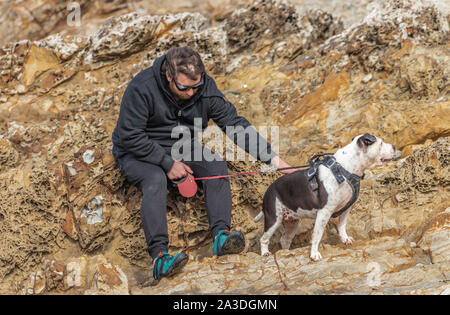 Mann sitzt auf Felsen mit Hund balanciert auf zu laufen Stockfoto