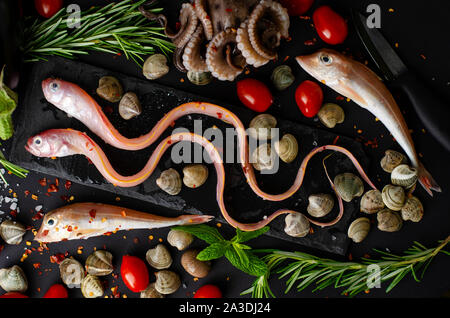 Frischer gemischter Meer Fisch, Tintenfisch, Tomaten und Rosmarin auf einer Grillpfanne auf dunklen bacground. Mediterran essen Konzept. Ansicht von oben Stockfoto