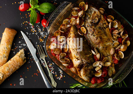 Brassen und Muscheln in transparenten Gericht frisch gebackenen im Ofen mit italienischen Brot gefüllt mit grünen Oliven auf dunklem Hintergrund. Ansicht von oben. Mediterranean cui Stockfoto