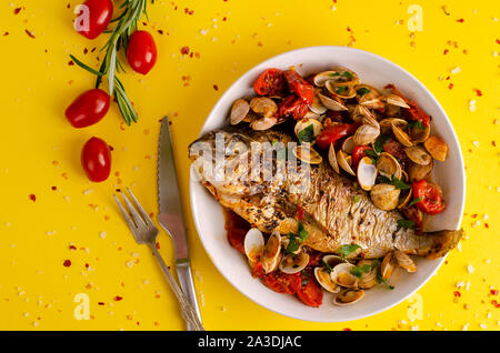 Meeresfrüchte Konzept. Dorada mit Muscheln in Tomaten sause im Ofen gebacken in einer weißen Schüssel auf gelben Hintergrund. Platz kopieren Stockfoto